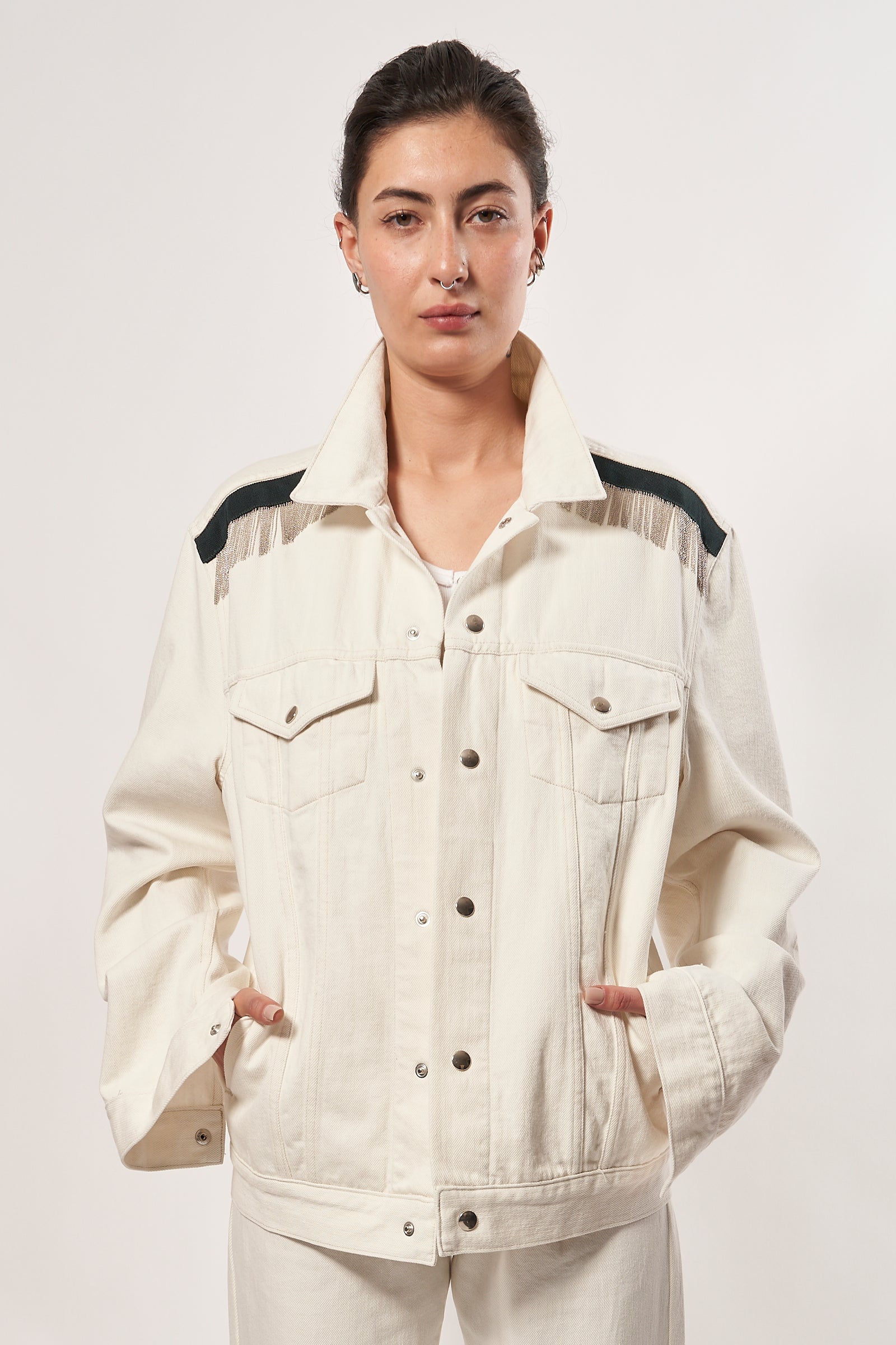 SARAH DE SAINT HUBERT ROMY CHAINS écru cotton denim jacket is the perfect blend of timeless design and modern style. Its signature hand-embroidered chains at the shoulders with dark green gros-grain tape and silver press buttons add a luxurious touch, giving it a boyish yet pure look. This jacket is sure to be your go-to for a timeless rock'n roll look. Limited edition Kara is 168 cm tall and wears a size M 100% cotton, Made in Portugal