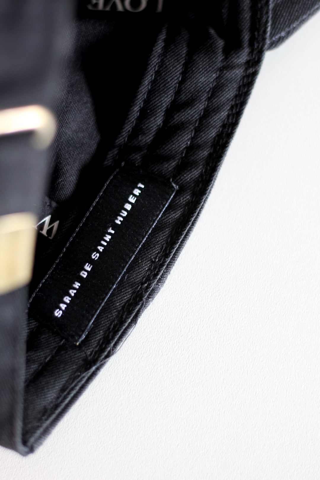 Black cotton baseball cap, 6 panels White 3-D embroidered SDSH monogram curved peak with 6 brim stitches reinforced 2 front panels adjustable fabric strap closure with metal buckle & loop inside printed tape 'FOLLOW YOUR WILD LOVE' 100% cotton twill