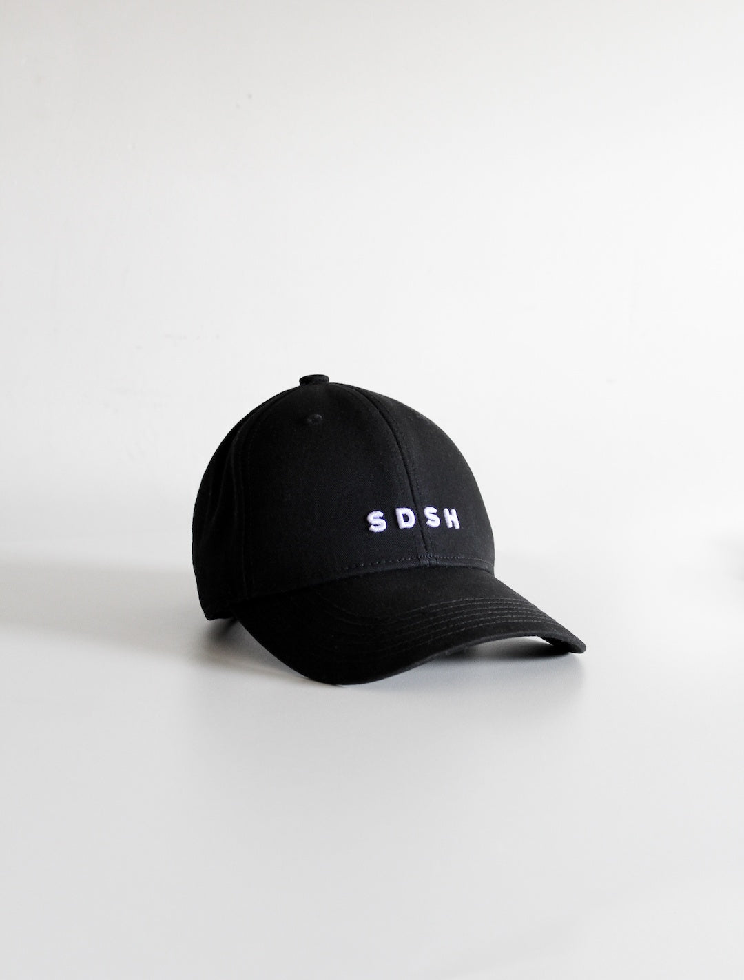 Black cotton baseball cap, 6 panels White 3-D embroidered SDSH monogram curved peak with 6 brim stitches reinforced 2 front panels adjustable fabric strap closure with metal buckle & loop inside printed tape 'FOLLOW YOUR WILD LOVE' 100% cotton twill
