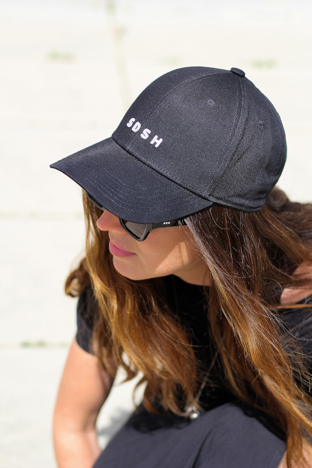 Black cotton baseball cap, 6 panels White 3-D embroidered SDSH monogram curved peak with 6 brim stitches reinforced 2 front panels adjustable fabric strap closure with metal buckle & loop inside printed tape 'FOLLOW YOUR WILD LOVE' 100% cotton twill