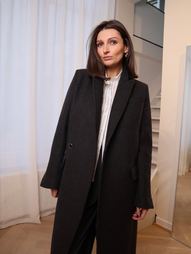 Crafted from 100% pure wool, this coat is a tribute to understated luxury. Its flowing silhouette whispers sophistication, enveloping you in warmth without compromise. Whether layered over tailored ensembles or paired with casual staples, it becomes an effortless extension of your style. A timeless piece designed for those who seek beauty in simplicity and grace in every step. Produced in Portugal in limited quantities.