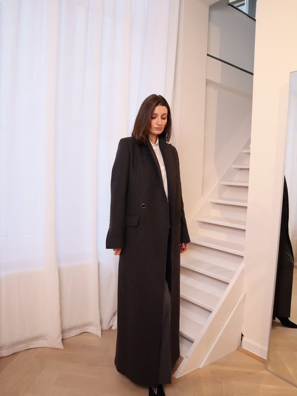 Crafted from 100% pure wool, this coat is a tribute to understated luxury. Its flowing silhouette whispers sophistication, enveloping you in warmth without compromise. Whether layered over tailored ensembles or paired with casual staples, it becomes an effortless extension of your style. A timeless piece designed for those who seek beauty in simplicity and grace in every step. Produced in Portugal in limited quantities.