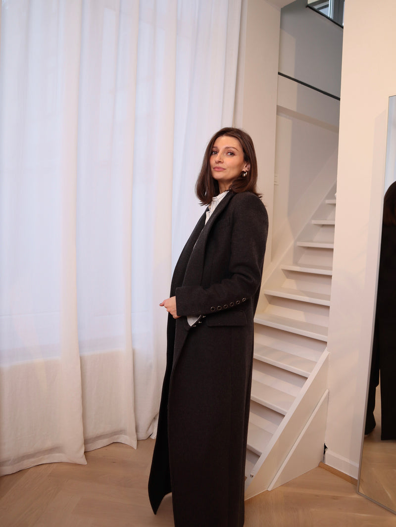 Crafted from 100% pure wool, this coat is a tribute to understated luxury. Its flowing silhouette whispers sophistication, enveloping you in warmth without compromise. Whether layered over tailored ensembles or paired with casual staples, it becomes an effortless extension of your style. A timeless piece designed for those who seek beauty in simplicity and grace in every step. Produced in Portugal in limited quantities.