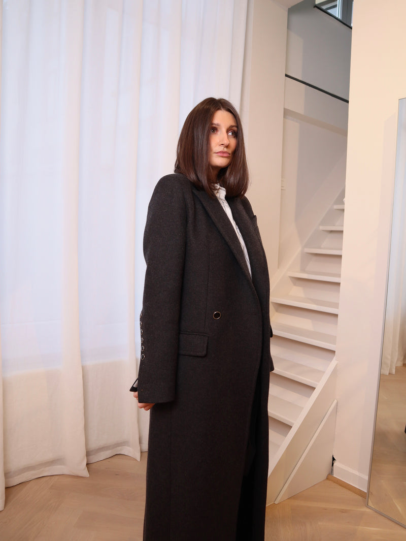 Crafted from 100% pure wool, this coat is a tribute to understated luxury. Its flowing silhouette whispers sophistication, enveloping you in warmth without compromise. Whether layered over tailored ensembles or paired with casual staples, it becomes an effortless extension of your style. A timeless piece designed for those who seek beauty in simplicity and grace in every step. Produced in Portugal in limited quantities.