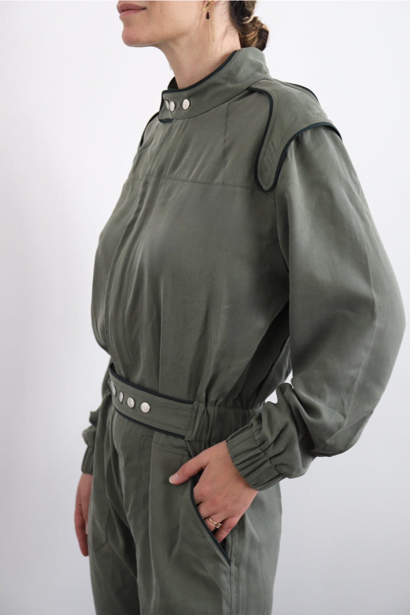 SARAH DE SAINT HUBERT Heritage racing jumpsuit with SDSH signature details. Dark green gros-grain trimming around the neck and waist belt. Iconic rows of metal snaps at the collar and waist. Wear it baggy for a boyish look. Wear it tightened at the waist for a more feminine look. Straight and relaxed fit. Khaki tencel (natural fibers). 100% tn. Designed in Belgium, Made in Portugal